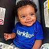 baby, child, smile, blue_shirt, curly_hair, car_seat, blanket, happy, face, infant, cute, clothing, person, portrait, indoor, young_child, hand, eyes, seat, baby_toddler