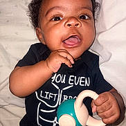 Sincere joined the competition — help win amazing prizes! baby, child, infant, smiling, happy, toy, black_clothing, shirt, face, hand, curly_hair, lying_down, blanket, indoors, cute, portrait, playful, skin, young, person