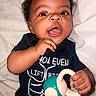 baby, child, infant, smiling, happy, toy, black_clothing, shirt, face, hand, curly_hair, lying_down, blanket, indoors, cute, portrait, playful, skin, young, person