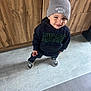 toddler, child, boy, beanie, hat, hoodie, sneakers, floor, tile, wooden_cabinet, indoor, smile, standing, clothing, casual, cute, portrait, person, headwear, happy