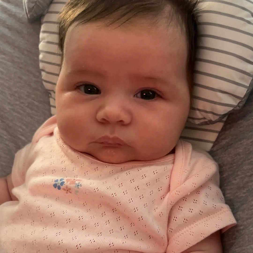 Brenna joined the competition — help win amazing prizes! baby, child, clothing, cute, expression, face, hair, indoors, infant, lying_down, newborn, onesie, person, pillow, pink, portrait, skin, soft, spiky_hair, striped