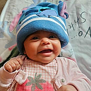 Camila joined the competition — help win amazing prizes! baby, smiling, hat, blue_hat, pink_clothing, blanket, cartoon_characters, face, happy, infant, cute, indoors, child, portrait, baby_clothes, hand, lying_down, text_background, cozy, closeup