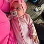 Maelys participe au concours pour gagner de l'argent avec cette photo : baby, pacifier, pink_clothing, headband, adult, wooden_floor, toy, hand, floor, indoor, person, infant, sleepwear, cuddling, cute, face, child, holding, comfort, relaxation