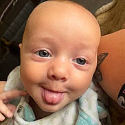 Jovanni joined the competition — help win amazing prizes! baby, face, tongue, blue_eyes, blanket, closeup, infant, skin, expression, person, tattoo, arm, playful, cute, child, indoors, soft_texture, smile, young, head