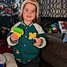 Sebastian joined the competition — help win amazing prizes! toddler, child, toy, hat, jacket, indoor, christmas_tree, living_room, curtains, couch, floor, wood_floor, smiling, person, plush_toys, decorations, socks, furniture, holiday, portrait