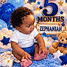 Zephaniah is registered to the contest to win money with this photo: baby, infant, child, portrait, sitting, curly_hair, smiling, toes, white_shirt, blue_shorts, teddy_bear, birthday, five_months, crown, balloons, stars, clouds, blue_blanket, nursery, indoor