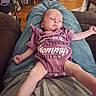 Naomi is registered to the contest to win money with this photo: baby, infant, onesie, purple_clothing, person, indoor, lap, relaxing, wood_floor, couch, jeans, home, casual, furniture, carpet, slippers, legs, hands, face, expression