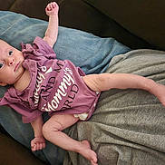 Naomi joined the competition — help win amazing prizes! baby, infant, onesie, purple_clothing, person, lap, cushion, fabric, indoor, skin, face, hand, foot, newborn, cute, lying_down, relaxed, small, child, human