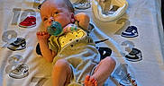 Naomi is registered to the contest to win money with this photo: baby, blanket, child, clothing, comfort, cute, fabric, footwear, headband, indoors, infant, lying_down, newborn, numbers, pacifier, pattern, person, small, sneakers, soft_toys