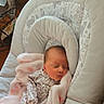 newborn, baby, sleeping, blanket, baby_seat, floral_clothing, soft_toys, indoors, natural_light, peaceful, infant, cushion, pink, cozy, resting, portrait, cute, child, comfort, household