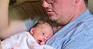 Naomi is registered to the contest to win money with this photo: baby, man, glasses, couch, blanket, indoor, person, holding, newborn, floral_pattern, tattoo, casual_clothing, home, family, affection, portrait, seated, closeup, love, comfort