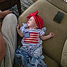 Naomi is registered to the contest to win money with this photo: baby, sleeping, couch, red_headband, blue_and_white_clothing, american_flag, smartphone, wooden_table, person, grey_pants, hand, floor, rug, living_room, furniture, indoor, cozy, relaxing, peaceful, infant