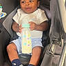 baby, car_seat, bottle, milk, white_tshirt, blue_shorts, navy_socks, nike_logo, infant, child, smiling, cute, happy, indoors, seat_belt, person, portrait, young, holding, sitting