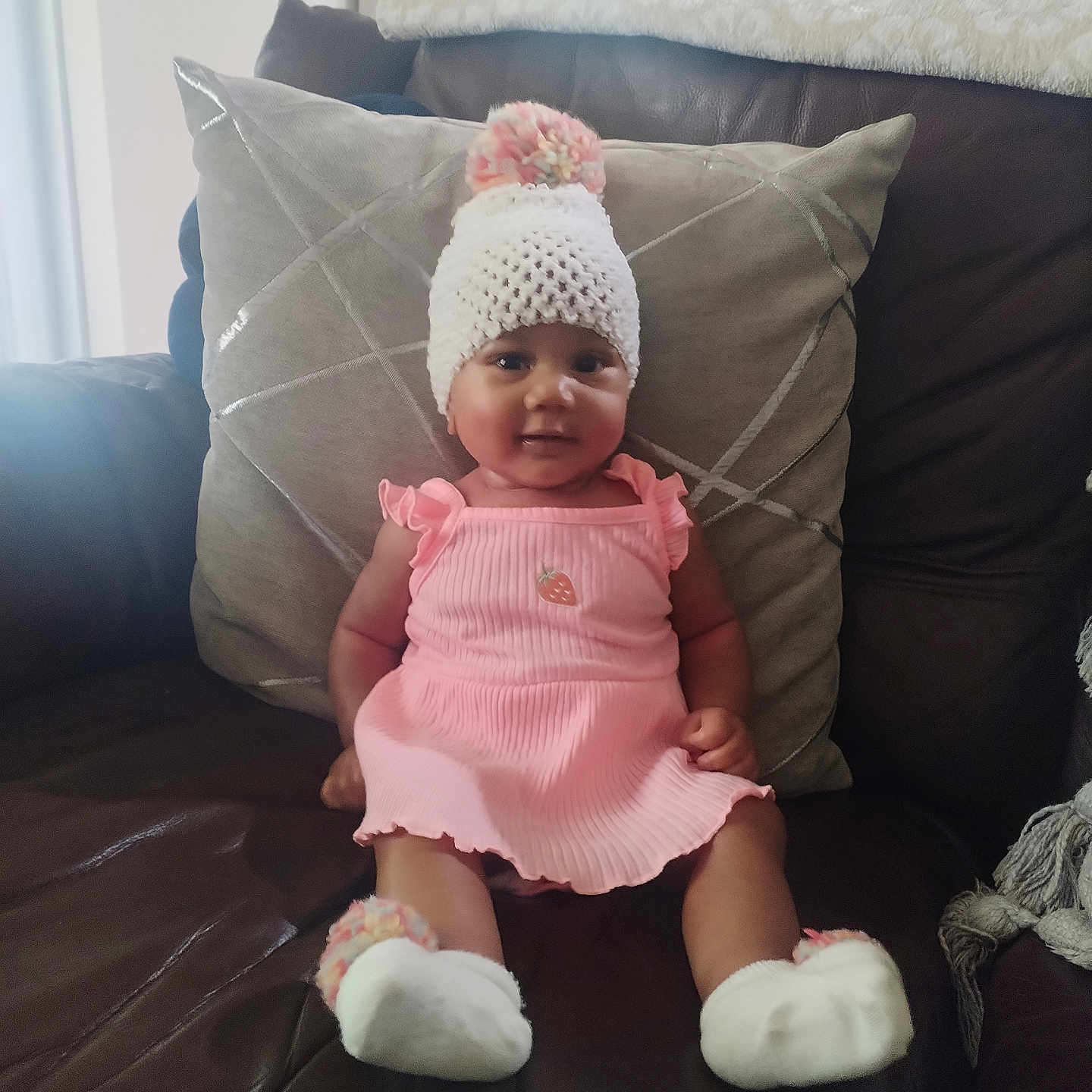 Sophia joined the competition — help win amazing prizes! baby, child, infant, sitting, sofa, couch, pillow, pink_outfit, knit_hat, pom_pom, fuzzy_slippers, portrait, indoors, living_room, leather, smiling, cute, fashion, cozy, photography