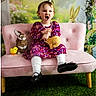 Hadley joined the competition — help win amazing prizes! black_shoes, child, cute, decorative_background, floral_dress, flowers, grass_carpet, happy, indoor, person, pink_couch, playful_expression, portrait, rabbit_toy, seated, smiling, stuffed_animal, toddler, white_tights, yellow_chick_toy