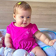Razane a rejoint le concours — aidez-le/la à gagner de superbes lots ! baby, bed, blanket, child, chubby_cheeks, cute, foot, hair_clip, happy, head, indoor, infant, person, pink_dress, seated, skin, smiling, soft_toys, stuffed_animal, toy