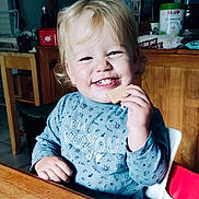 Samuel a rejoint le concours — aidez-le/la à gagner de superbes lots ! toddler, child, smiling, cookie, high_chair, blonde_hair, blue_shirt, kitchen, wooden_table, happy, indoor, person, food, snack, cute, sitting, young_child, face, portrait, meal