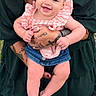 baby, child, infant, smiling, portrait, headband, bow, ruffled_clothing, pink_outfit, denim, tattoos, adult, parent, arms, outdoor, grass, memorial_plaque, engraving, sitting, happy