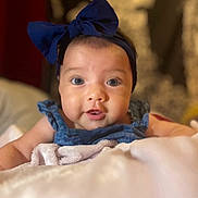 Leilani is registered to the contest to win money with this photo: baby, infant, child, portrait, close_up, face, wide_eyes, looking_at_camera, bow, headband, blue_clothing, denim, blanket, bed, indoors, soft_lighting, cozy, sitting, cute, photography
