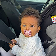 Aria participe au concours pour gagner de l'argent avec cette photo : baby, car, car_interior, car_seat, child, curly_hair, cute, indoors, infant, knitwear, looking, pacifier, person, portrait, safety, seat, seatbelt, sitting, white_clothing, young_child