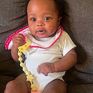 Kyomi is registered to the contest to win money with this photo: baby, infant, child, pacifier, onesie, bib, couch, blanket, sitting, indoors, cute, face, expression, hand, footwear, soft_furniture, comfort, young, portrait, skin