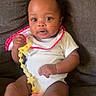 baby, infant, child, pacifier, onesie, bib, couch, blanket, sitting, indoors, cute, face, expression, hand, footwear, soft_furniture, comfort, young, portrait, skin