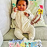 Tyler is registered to the contest to win money with this photo: baby, infant, onesie, couch, pillow, floral_pillow, happy_easter_sign, holiday, celebration, indoors, smiling, cute, child, portrait, soft_lighting, decor, colorful_sign, cozy, seated, young_child
