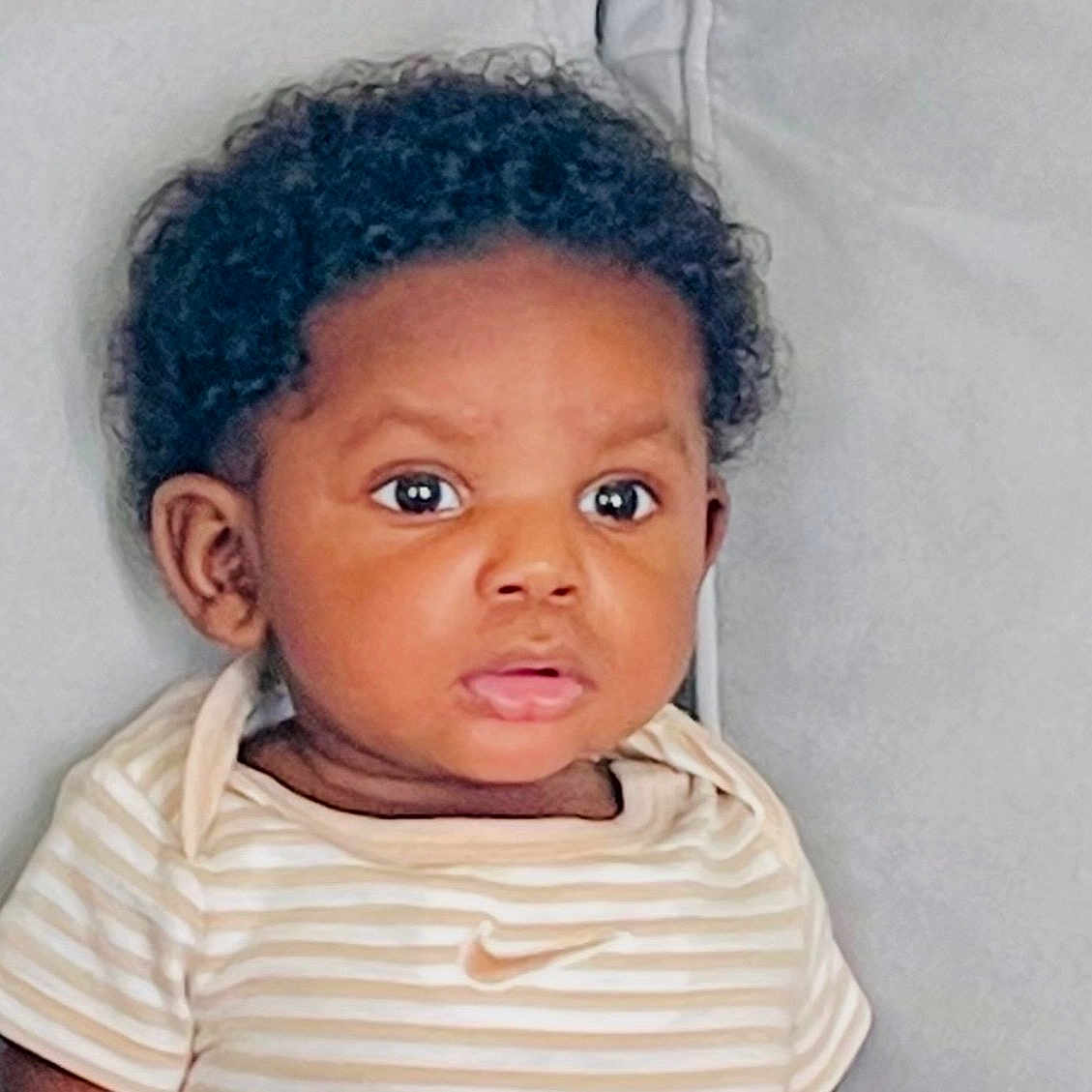 Tyler joined the competition — help win amazing prizes! baby, child, curly_hair, striped_clothing, nike_logo, portrait, indoor, face, cute, expression, infant, young_child, sitting, soft_background, closeup, person, eyebrows, eyes, lips, head