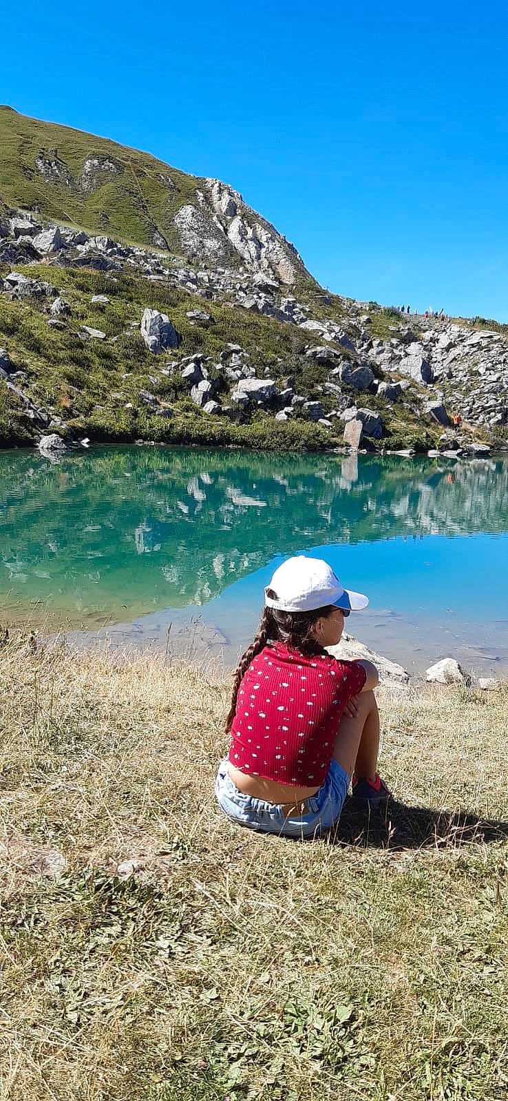 Clara participe au concours pour gagner de l'argent avec cette photo : bank, fun, grass, highland, hill, lake, landscape, leisure, mountain, mountain_range, natural_landscape, people_in_nature, person, plant, recreation, sky, sun_hat, tarn, travel, valley