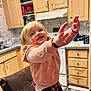 child, toddler, bubble, kitchen, hoodie, smiling, blonde_hair, indoor, cabinet, dishwasher, countertop, chair, playful, happy, reaching, floral_pants, home, cute, person, fun