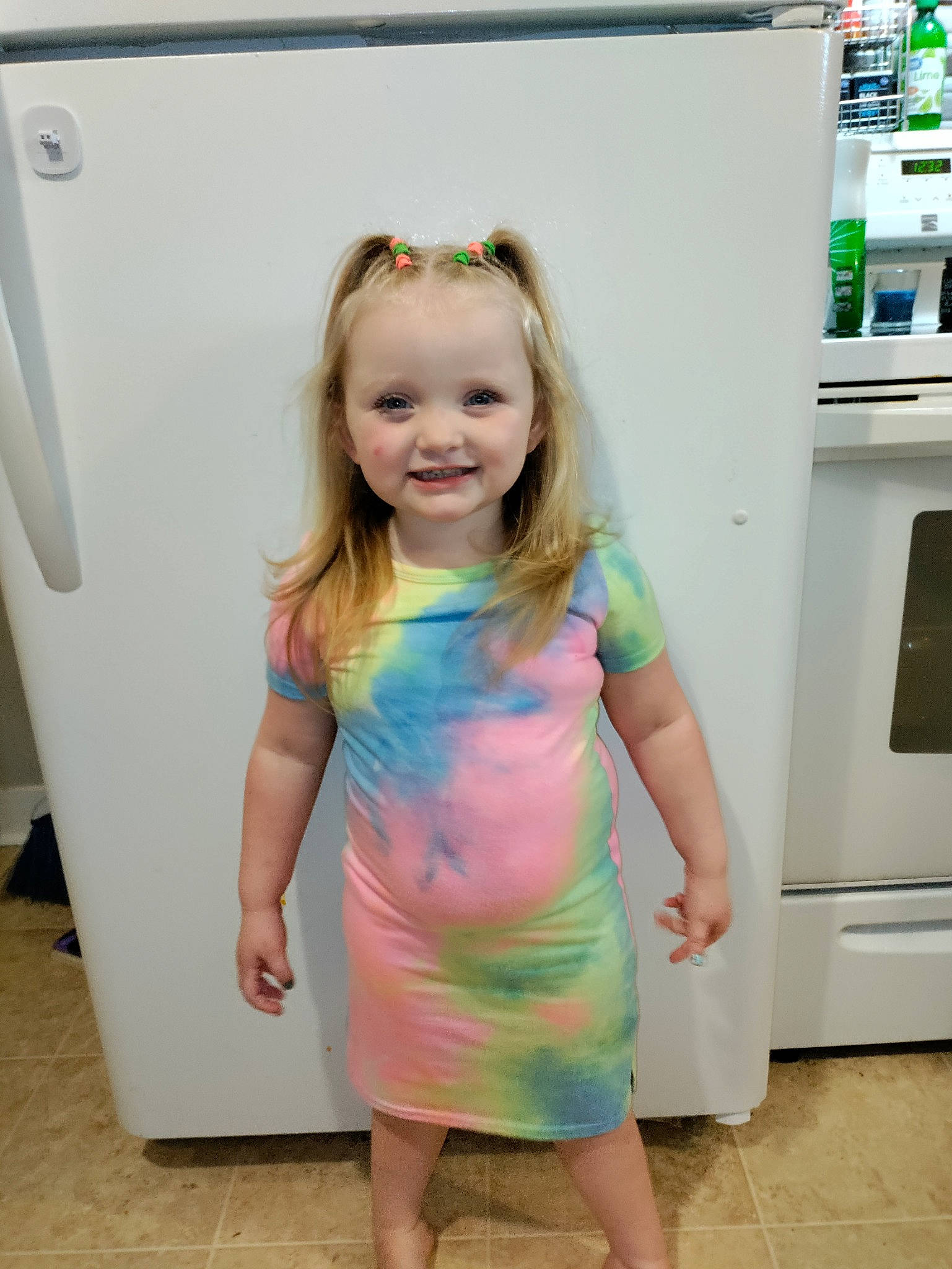 Dayona is registered to the contest to win money with this photo: baby_toddler_clothing, blond, cabinetry, child, facial_expression, fun, happy, joint, joy, kitchen_appliance, one_piece_garment, person, pink, purple, room, shoulder, sleeve, smile, snapshot, standing