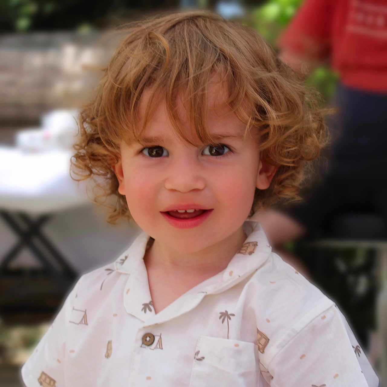 Noah participe au concours pour gagner de l'argent avec cette photo : blurred_background, casual_clothing, child, curly_hair, cute, daylight, face, family, happy, nature, outdoor, people, person, portrait, seated, shirt, smiling, table, toddler, young_child
