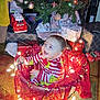 baby, child, christmas_tree, christmas_lights, holiday, pajamas, basket, presents, gift_wrap, festive, decorations, smiling, indoor, floor, carpet, toy, red, green, celebration, happy