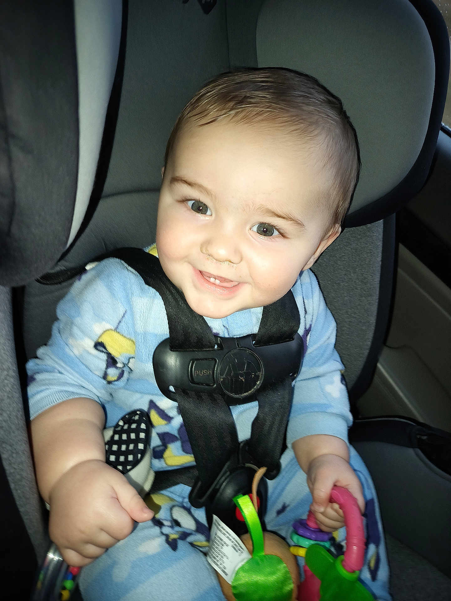 Kayson is registered to the contest to win money with this photo: baby, child, car_seat, safety_harness, smiling, pajamas, toy, indoor, seatbelt, cute, infant, person, car_interior, happy, face, young_child, holding, closeup, seat, play