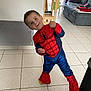 child, boy, spiderman_costume, playful, indoor, living_room, couch, chair, tile_floor, costume, pose, curtain, furniture, home, casual, smile, person, clothing, footwear, fun