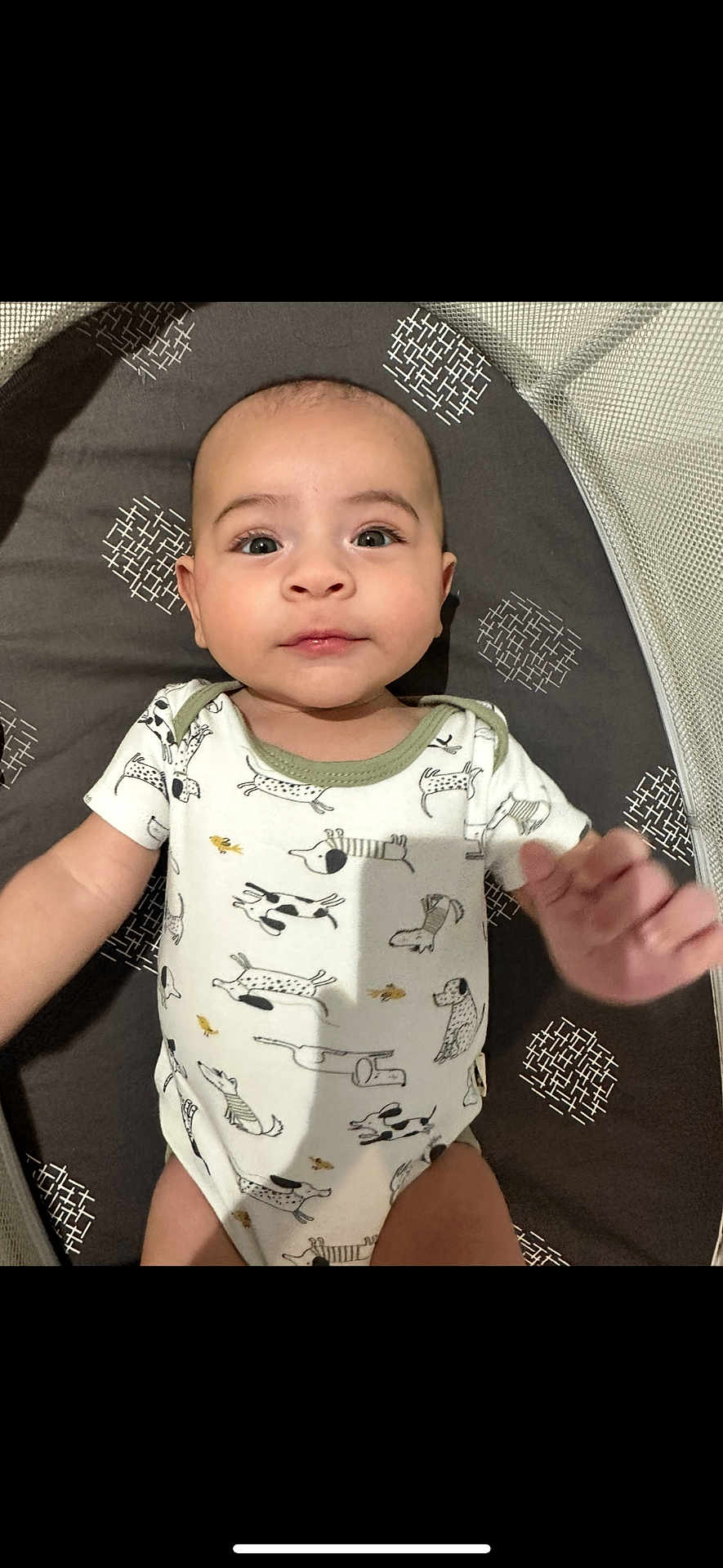 Jax is registered to the contest to win money with this photo: baby, infant, onesie, dog_print, patterned_mat, lying_down, face, hand, cute, child, portrait, indoors, expression, looking_at_camera, skin, head, eyes, mouth, person, baby_clothing
