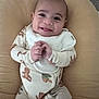 baby, smile, onesie, bib, teddy_bear_pattern, cushion, infant, happy, hands, clasped_hands, cute, lying_down, soft_texture, indoor, child, young, portrait, cozy, comfortable, clothing