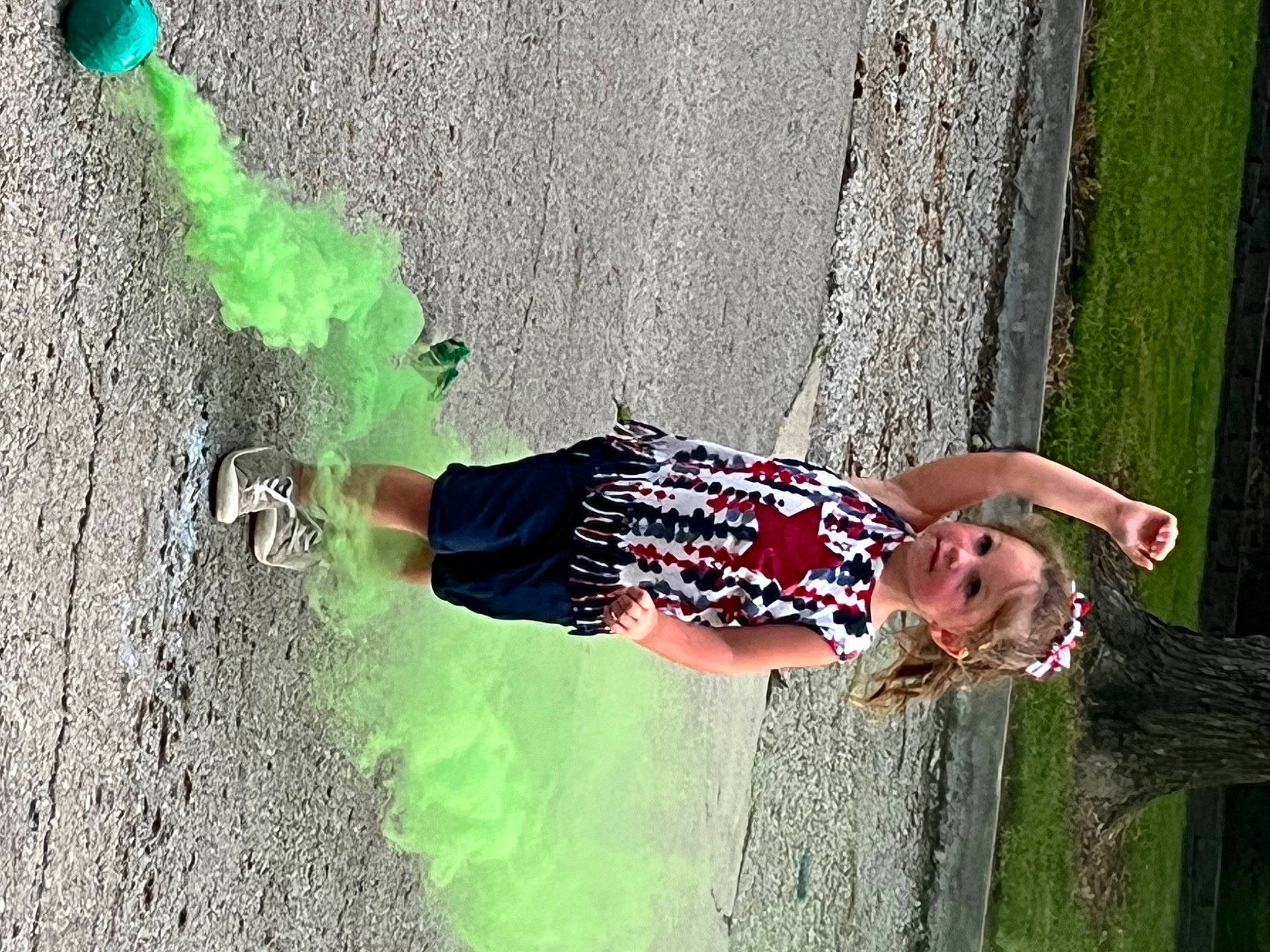 Emma is registered to the contest to win money with this photo: asphalt, fun, grass, green, happy, human_leg, leg, leisure, people, people_in_nature, person, plant, recreation, shadow, smile, tints_and_shades, toddler, tree, waist, wall