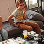 Tiago a rejoint le concours — aidez-le/la à gagner de superbes lots ! child, children, kid, sitting, sofa, couch, cup, drink, chocolate, snack, table, pillow, glasses, jeans, t_shirt, game_controller, cables, checkerboard_wall, floor_tiles, remote_control