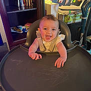 Kyrsten is registered to the contest to win money with this photo: artwork, baby, child, clothing, dvd, face, furniture, hands, happy, high_chair, home, indoor, person, room, seat, shelf, smile, table, toy, wall