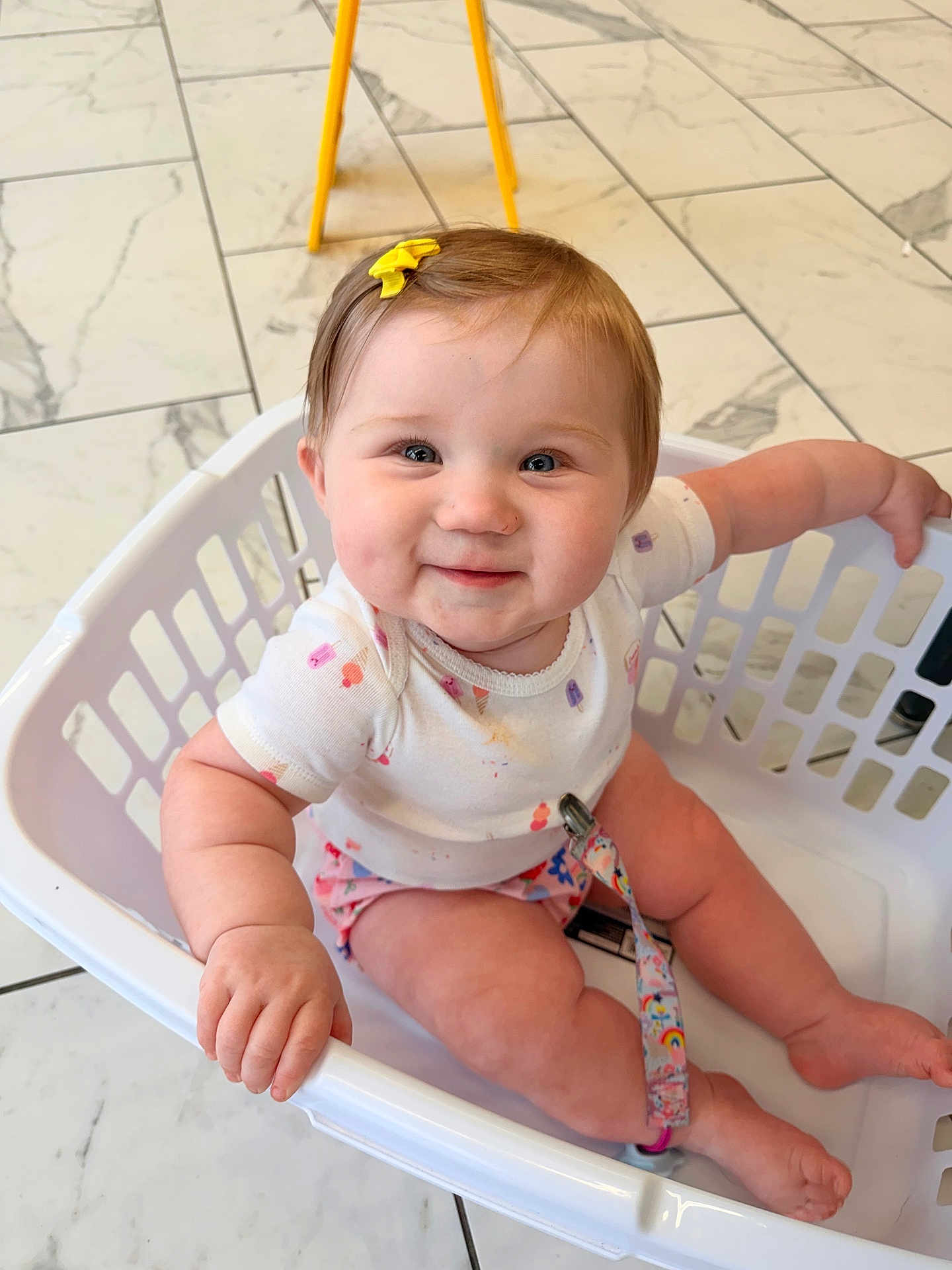Christina is registered to the contest to win money with this photo: baby, child, infant, smile, laundry_basket, basket, onesie, hair_bow, pacifier_clip, tiles, tile_floor, indoor, sitting, hand, legs, cheeks, face, cute, happy, photography