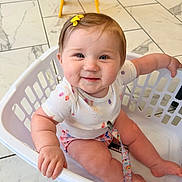 Christina is registered to the contest to win money with this photo: baby, child, infant, smile, laundry_basket, basket, onesie, hair_bow, pacifier_clip, tiles, tile_floor, indoor, sitting, hand, legs, cheeks, face, cute, happy, photography