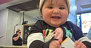 Kylie joined the competition — help win amazing prizes! baby, child, smiling, beanie, indoor, restaurant, sign, number, happy, face, person, clothing, cute, joyful, hand, table, menu, background, light, casual