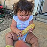 Kylie is registered to the contest to win money with this photo: baby, child, corn, corn_cob, hair, messy_hair, onesie, socks, outdoor, concrete, building, door, hose, curious, sitting, dirty, face, hands, food, footwear