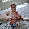 toddler, child, pacifier, smartphone, bed, blanket, window, blinds, red_bow, onesie, socks, indoor, person, furniture, light, shadow, cute, curious, baby, playful