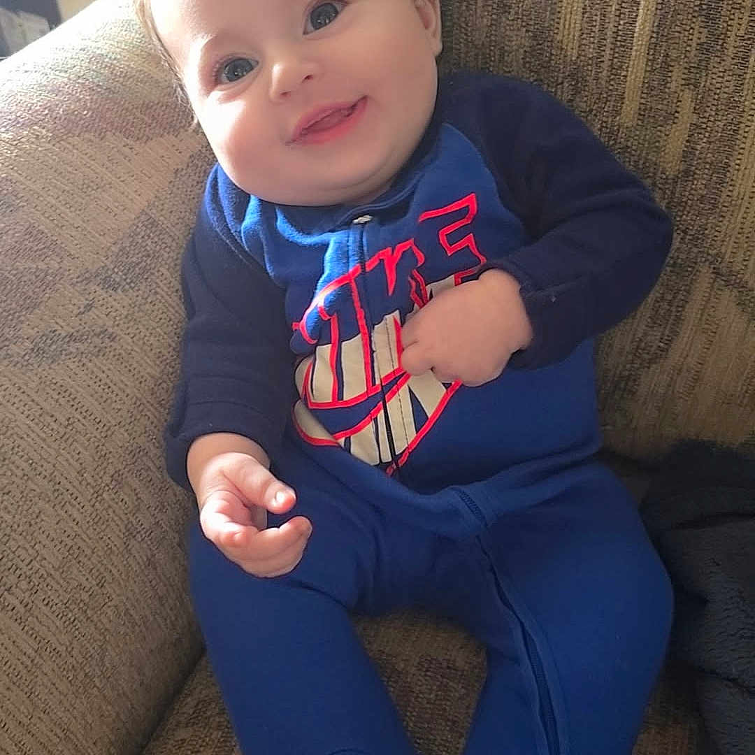 Rukia is registered to the contest to win money with this photo: baby, blue_onesie, child, couch, cozy, cute, face, footed_pajamas, furniture, hand, happy, home, indoor, infant, person, portrait, relaxed, seated, smiling, young_child
