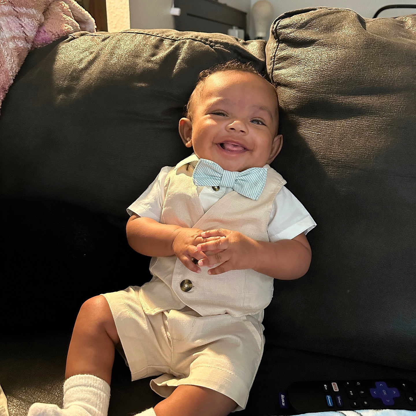 Jayceon is registered to the contest to win money with this photo: baby, blanket, bow_tie, casual, child, clothing, couch, cute, happy, home, indoor, infant, leather, person, remote_control, seated, shorts, smile, socks, vest