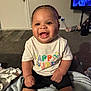 baby, smiling, happy, child, toddler, indoor, clothing, shirt, blanket, carpet, living_room, person, cute, sitting, expression, furniture, television, shorts, skin, joy