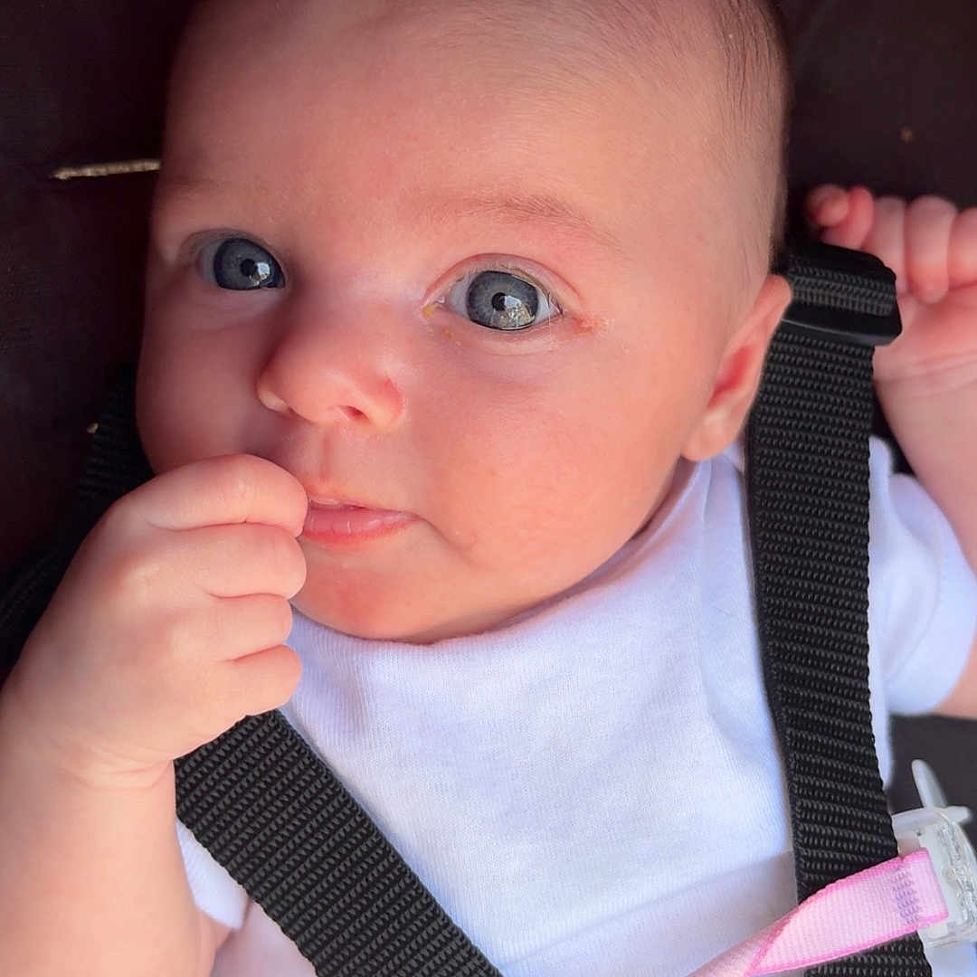 Summer is registered to the contest to win money with this photo: baby, infant, child, face, blue_eyes, hand, onesie, harness, straps, pacifier, pink_clip, skin, expression, closeup, portrait, cute, young, person, seated, indoor
