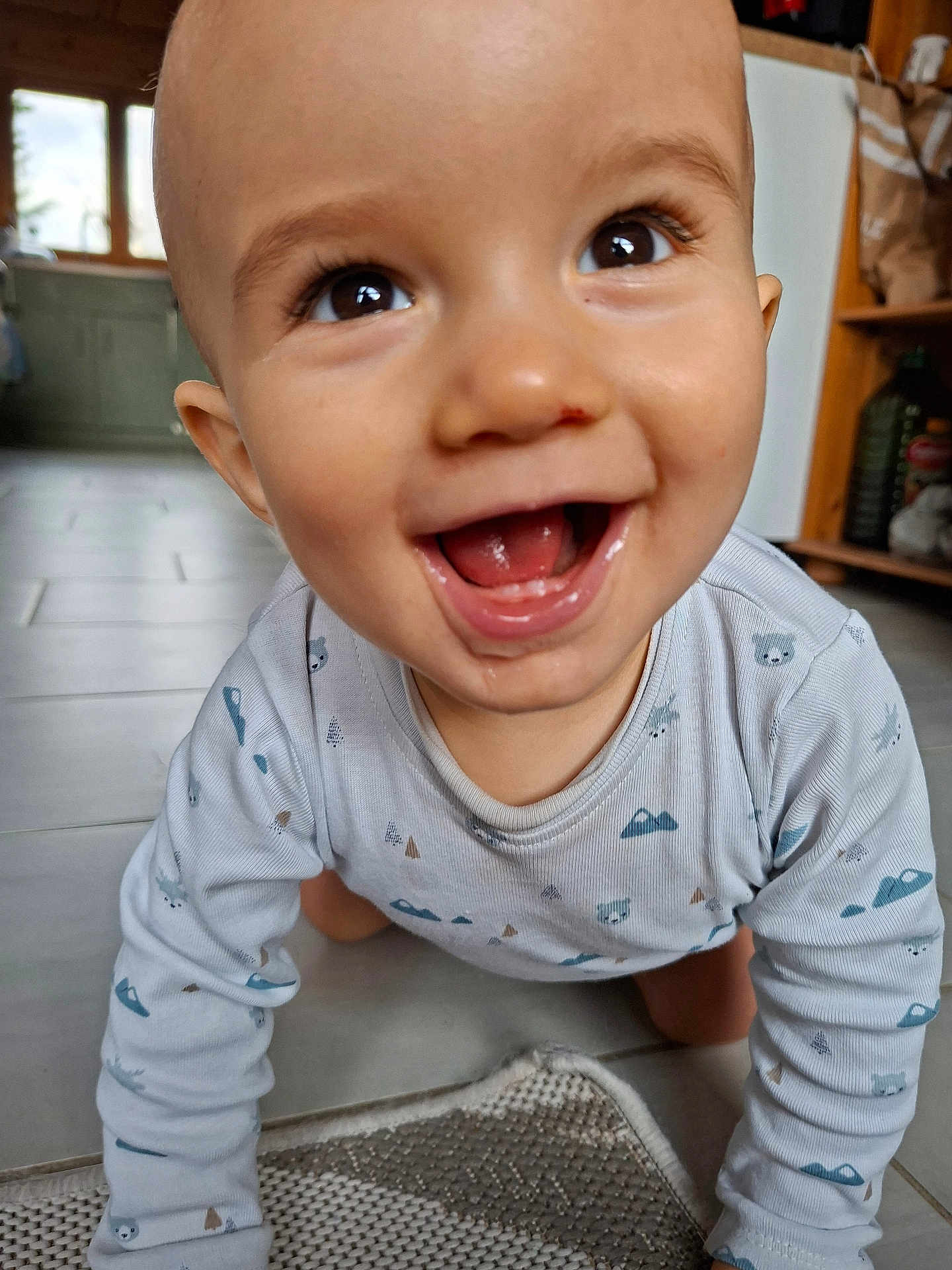 Charly participe au concours pour gagner de l'argent avec cette photo : baby, smiling, crawling, indoor, onesie, floor, happy, child, face, eyes, mouth, tongue, long_sleeve, patterned_clothing, home, kitchen, tile_floor, carpet, person, cute